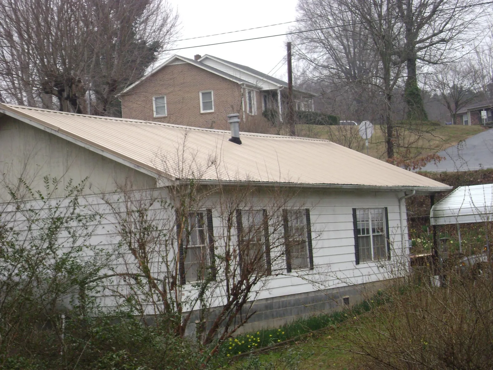Tan metal roof on a white sided house set into a hillside — Commercial Roofing by Roofing Brothers in Northampton