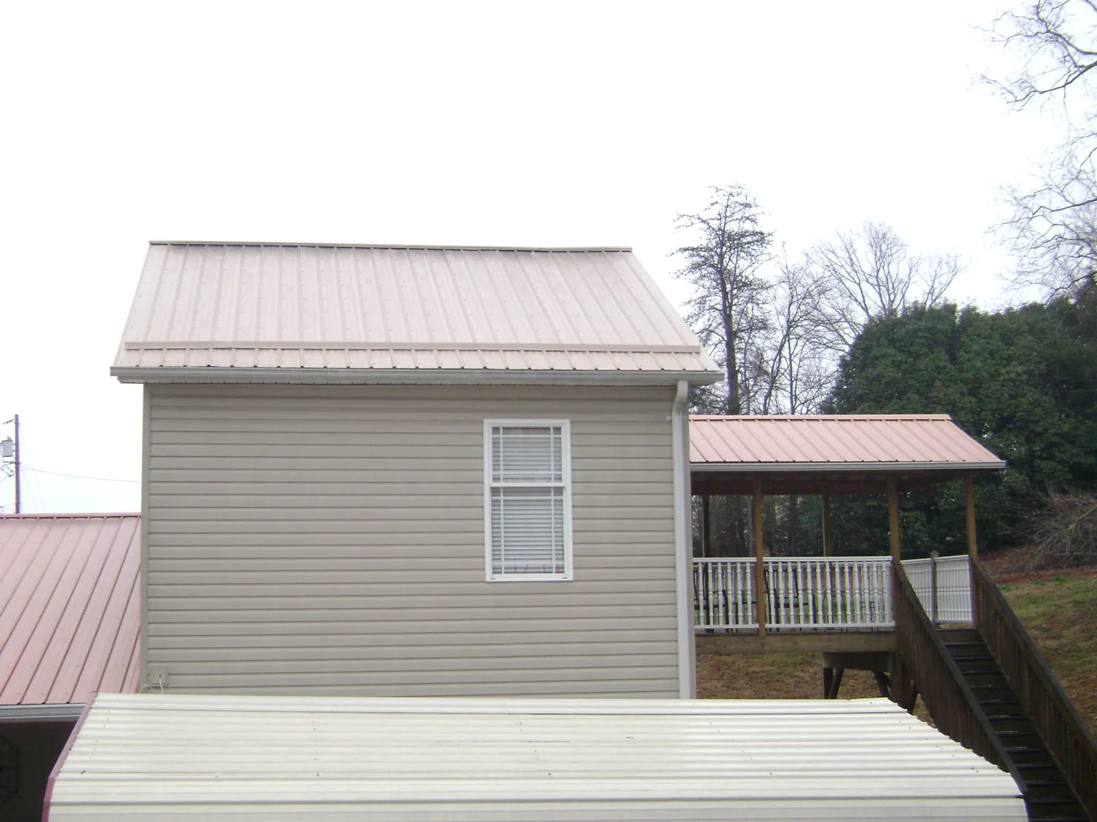 Tan metal roofs on a two story addition and attached porch, from a Roof Replacement job in Northampton